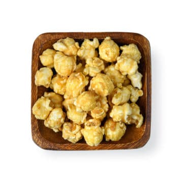 Decadent Popinsanity Banana Pudding popcorn, a dairy-free gourmet treat, captured in a square wooden bowl, emphasizing its appealing texture and color.