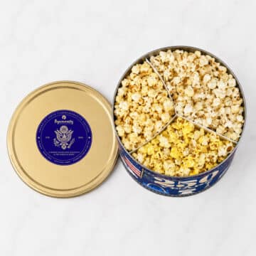 Aerial view of Popinsanity Americas 250th Commemorative Edition popcorn tin displaying three divided flavor sections next to a gold lid.